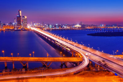 Illuminated light trails on bridge over city against sky at night