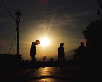 Silhouette teenagers with skateboard against sun during sunset