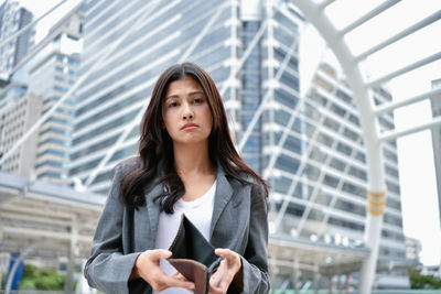 Portrait of tensed woman showing empty wallet against building in city