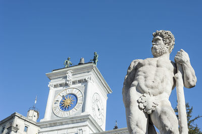 Low angle view of statue with built structure against blue sky