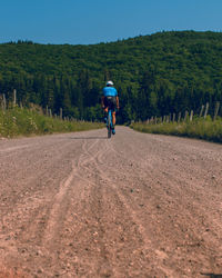 Rear view of man riding bicycle on dirt road against mountain