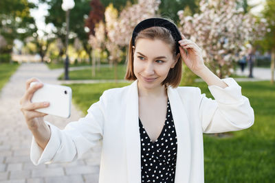 Young woman taking selfie with smart phone while standing in park