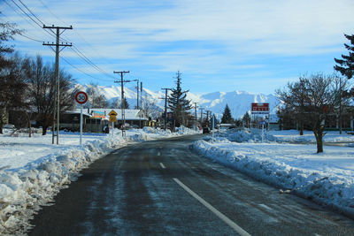 Road by trees against sky during winter