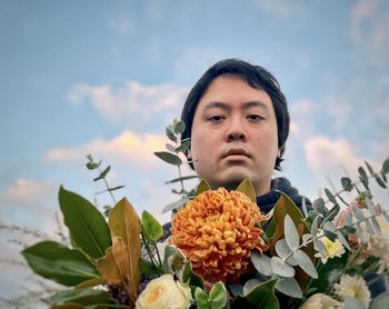 Portrait of young asian man with bouquet against blue sky.
