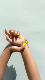 Woman with nail polish raising hands against wall