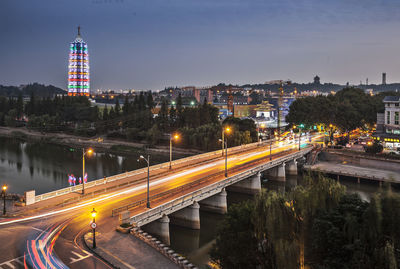 Light trails on bridge in illuminated city at dusk