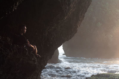 Man sitting on rock formation in sea