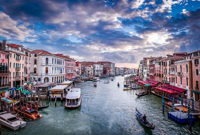 Boats on canal amidst buildings against cloudy sky