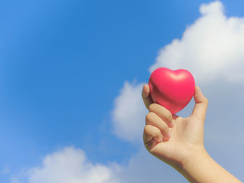 Close-up of hand holding heart shape balloon against blue sky