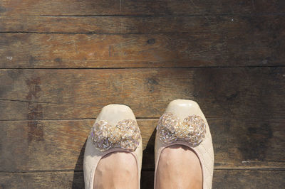 Low section of woman wearing shoes standing on wooden floorboard