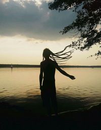 Silhouette of woman standing by lake against sky