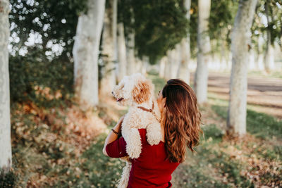 Rear view of woman carrying dog while standing outdoors