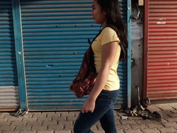 Side view of young woman standing against shutter