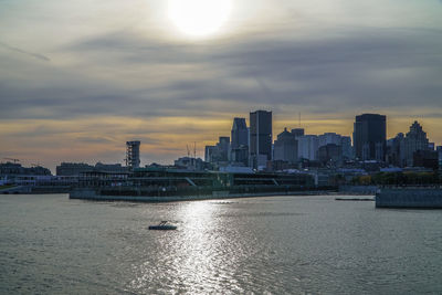 Sea by cityscape against sky during sunset