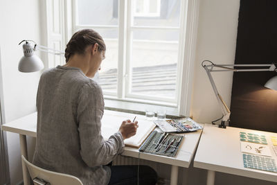 Artist painting on canvas against window in creative office