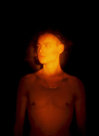 Young shirtless man sitting against black background