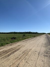 Dirt road amidst field against clear blue sky