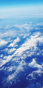 Aerial view of snowcapped mountains against blue sky
