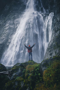 Man standing on rock against waterfall