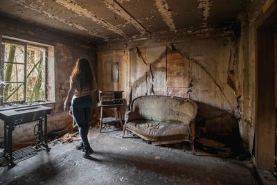 Woman standing by window of an abandoned house