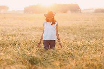 Rear view of woman wearing hat standing on field