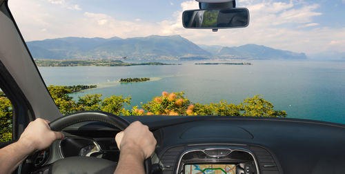 Cropped hands of man driving car against sea