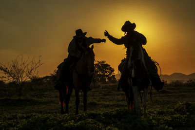 People riding horse on field against sky during sunset