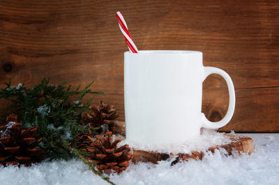 Close-up of candy cane in mug by twigs and pine cones amidst fake snow on table