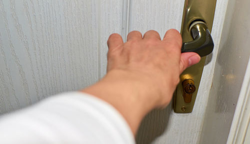 Close-up of a hand holding handler of a white door at the moment of opening it