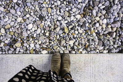 Low section of woman standing by pebbles on footpath