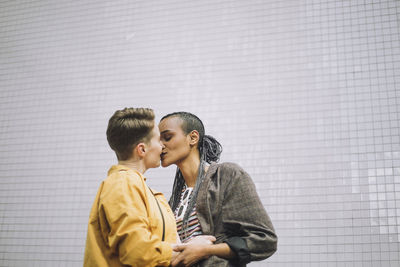 Young woman with eyes closed kissing girlfriend while standing against wall