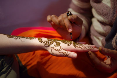 Midsection of woman applying henna on cropped hand