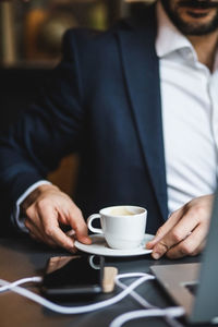 Midsection of man holding coffee cup on table