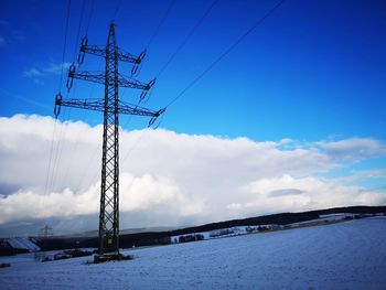 Low angle view of electricity pylon against sky during winter