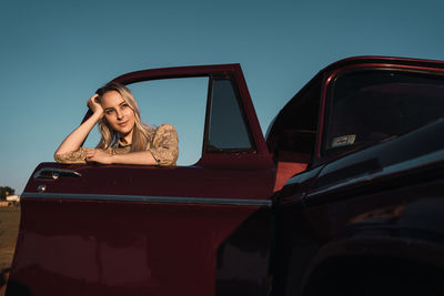 Low angle of cheerful female sticking out of car window and enjoying freedom in summer evening