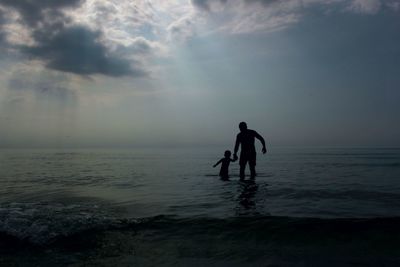 Silhouette man and child on beach against sky