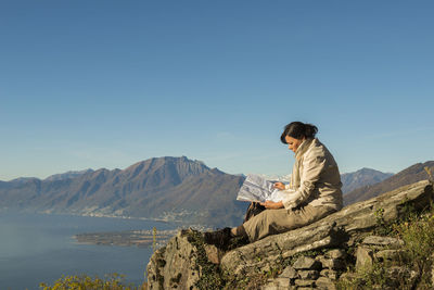 Side view of female hiker with map sitting on cliff against swiss alps