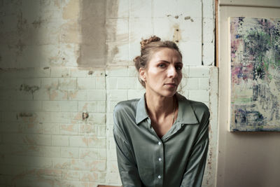 Confident artist sitting by painting in front of brick wall at studio