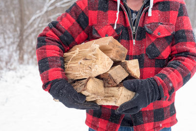 Midsection of man carrying logs on field during winter