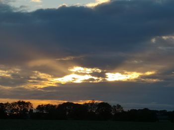 Silhouette trees against dramatic sky during sunset