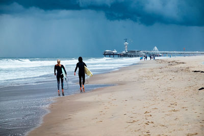 Rear view of surfers walking on shore at beach