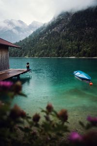 Woman sitting by stilt house over lake against sky