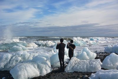 Rear view of people taking photos of ice formations in sea