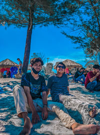 Friends sitting on land against blue sky