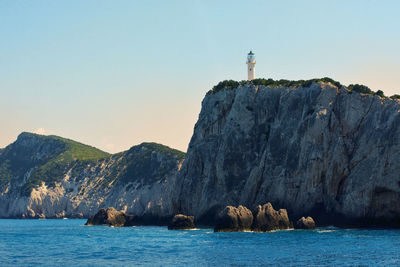 Lighthouse on rock by sea against clear sky