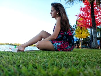 Young woman looking away while sitting on field