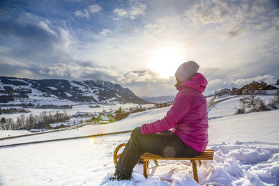 Man sitting on snowcapped mountain against sky