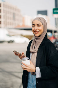 Portrait of smiling young woman using mobile phone in city