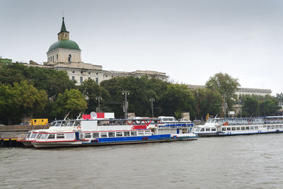 Boats in river by building against sky