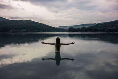 Rear view of woman with arms outstretched in lake against mountains